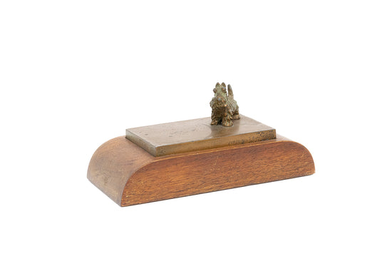 Small bronze-plated spaniel dog sculpture stands atop a bronze and wooden paperweight